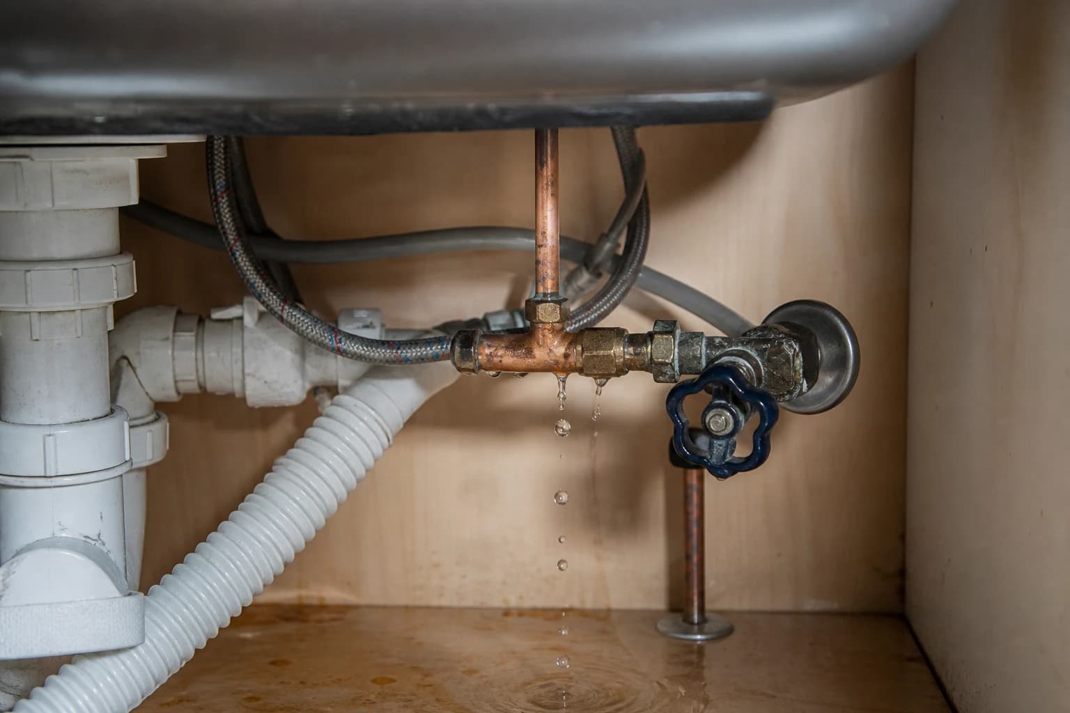 Water dripping from a copper pipe connection beneath a kitchen sink