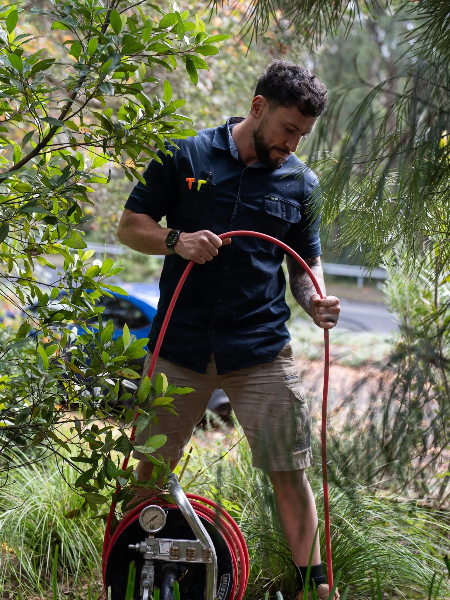 Tom Malone handling a drain-clearing hose beside garden plants