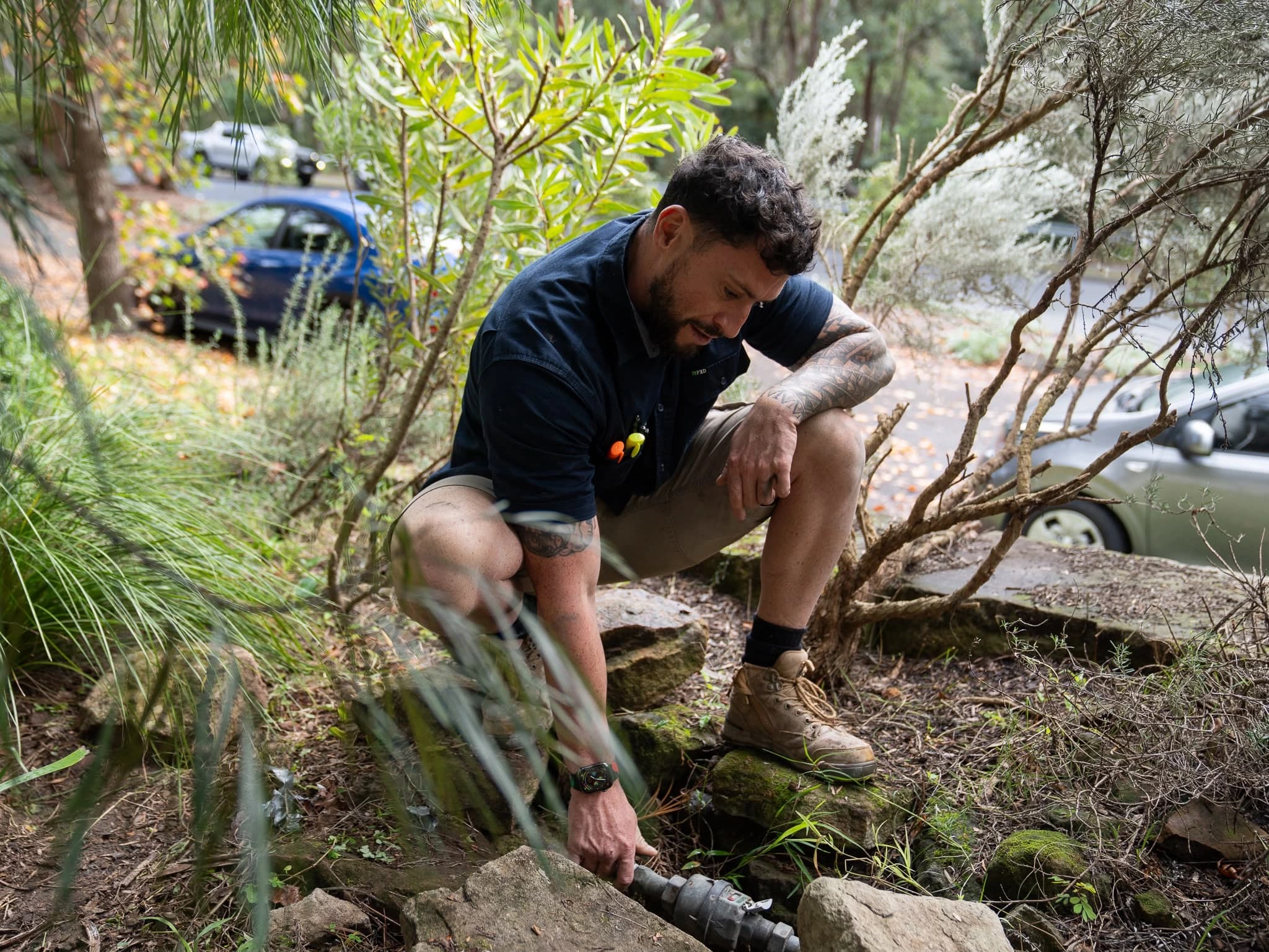 Tom Malone inspecting an outdoor pipe connection among garden plants